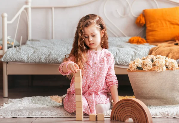 Plastik olmayan tahta oyuncaklar konsepti. Güzel küçük kız çocuk odasında tahta oyuncakla oynuyor.