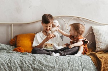 Küçük kız ve erkek kardeşler sabahları yatakta oturup eğleniyorlar. Kardeşler birlikte vakit geçirip rahatlıyorlar..