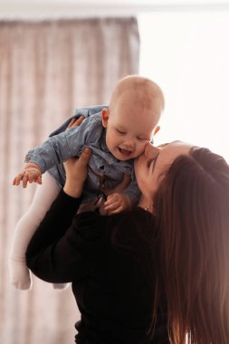 Evde genç anne kızını öpüyor, bakıcılık yapıyor, bebeği kucağına alıyor.