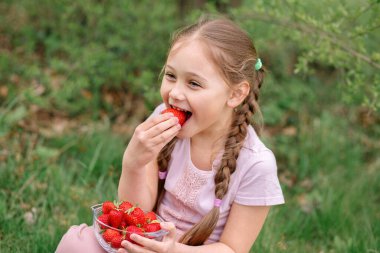 Mutlu küçük kızın portresi yaz günü çilek yiyor. Yumuşak odaklı