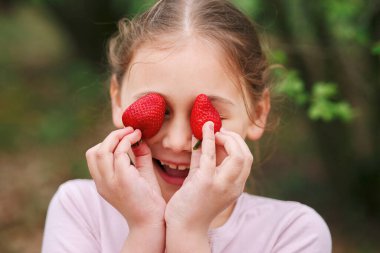 Mutlu küçük kızın portresi yaz günü çilek yiyor. Yumuşak odaklı