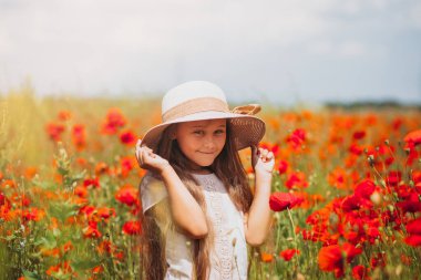 Uzun saçlı küçük kız yaz güneşinde haşhaş tarlasında poz veriyor.