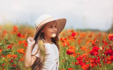 Uzun saçlı küçük kız yaz güneşinde haşhaş tarlasında poz veriyor.