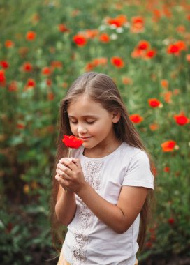 Yaz güneşinde haşhaş tarlasında poz veren uzun saçlı küçük kız. Dikey