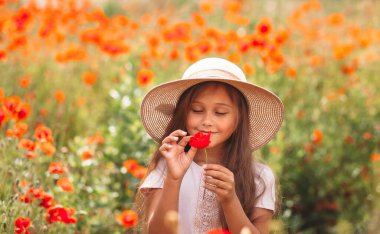 Uzun saçlı küçük kız yaz güneşinde haşhaş tarlasında poz veriyor.