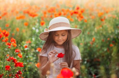 Uzun saçlı küçük kız yaz güneşinde haşhaş tarlasında poz veriyor.
