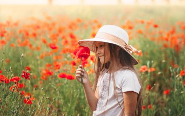Uzun saçlı küçük kız yaz güneşinde haşhaş tarlasında poz veriyor.