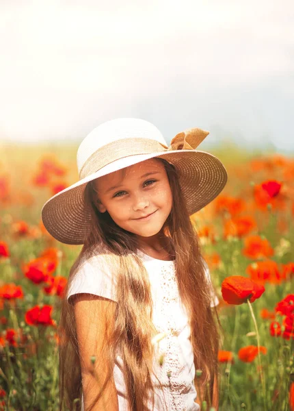 Uzun saçlı küçük kız yaz güneşinde haşhaş tarlasında poz veriyor.