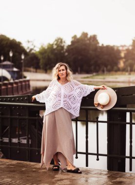 Beautiful blond young woman wearing  dress and straw hat enjoying sunrise on seafront in old european town. Fashion and style. Summer travel