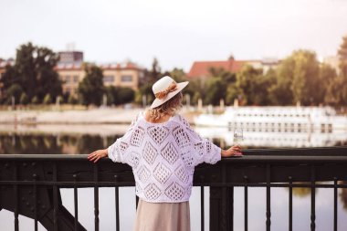 Young woman tourist standing with glass of white wine at bridge in european city , river at background