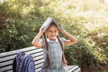 Girl with a backpack sitting on a bench and holds  books near the school. Back to school, lesson schedule, a diary with grades. Education, primary school classes, Back to school