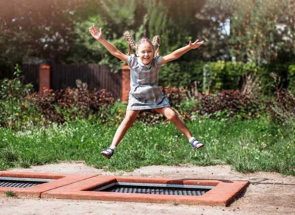 Little girl  is jumping on trampoline in a park. Happy laughing kid outdoors in the yard on summer vacation. Jump high