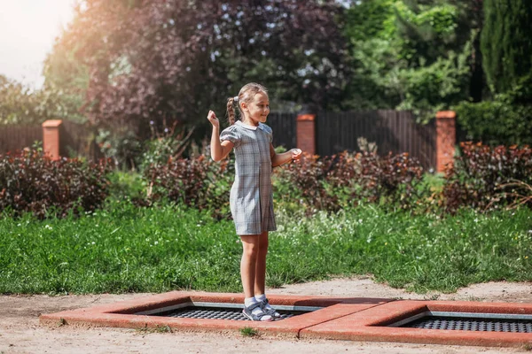 Little girl  is jumping on trampoline in a park. Happy laughing kid outdoors in the yard on summer vacation. Jump high