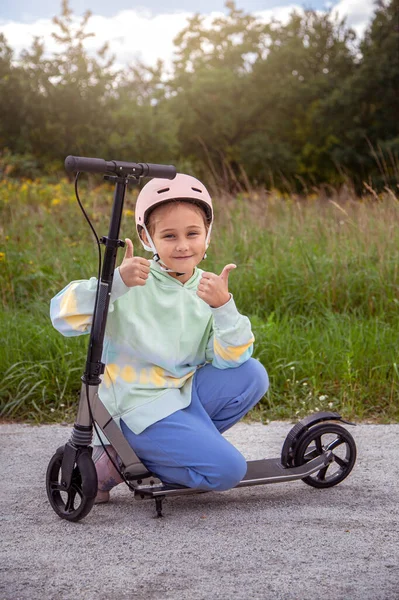  Güneşli bir günde, sokak parkında asfaltlı pistte motosiklet sürerken kask takan beyaz bir kızın portresi. Sağlıklı spor çocuk aktiviteleri