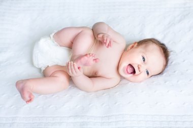 Laughing baby wearing a diaper playing with her feet