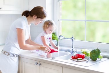 Mother and her daughter washing vegetables clipart