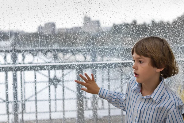 Cute boy standing next to a wet window