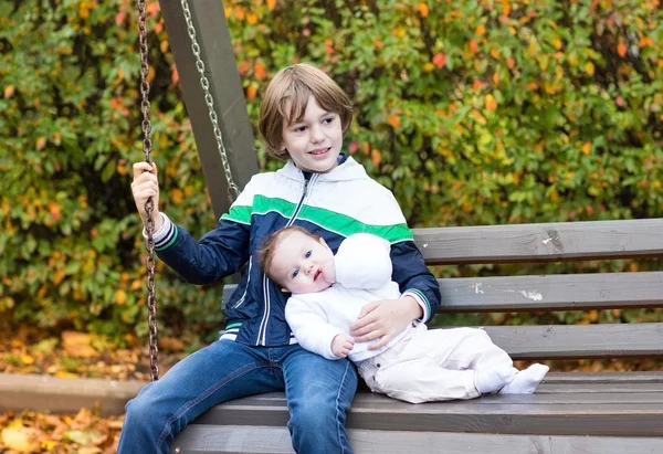 Junge und seine kleine Schwester entspannen sich auf einer Schaukel — Stockfoto