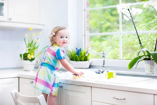 Fille laver la vaisselle, nettoyer avec une éponge et jouer avec la mousse — Photo