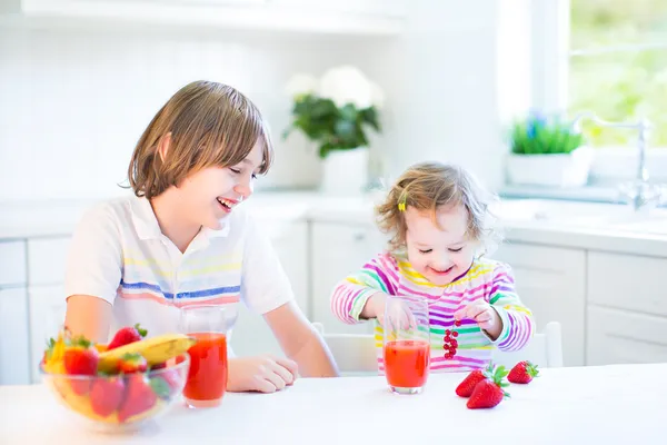 Gelukkig tiener jongen en zijn schattig peuter zus met fruit voor het ontbijt — Stockfoto