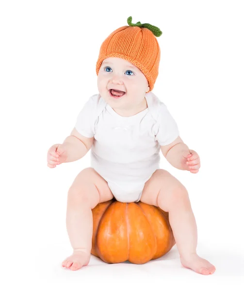 Baby girl playing with a huge pumpkin wearing a knitted pumpkin hat — Stock Photo, Image