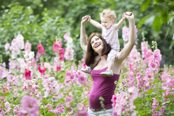 Zwangere moeder spelen met haar baby dochter in een in een bloeiende tuin — Stockfoto