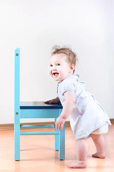 Baby girl standing next to a blue chair — Stock Photo, Image