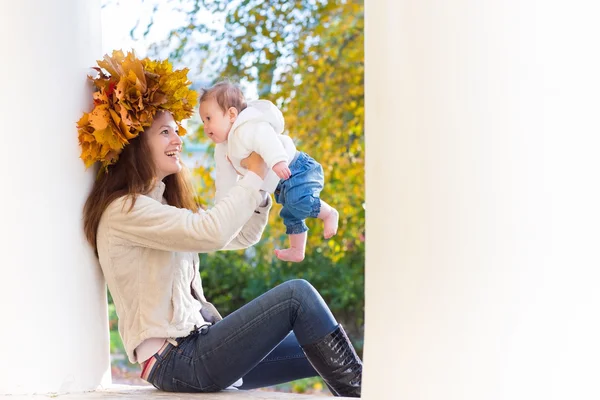 Woman with maple leaves wreath playing with her baby — Stock Photo, Image