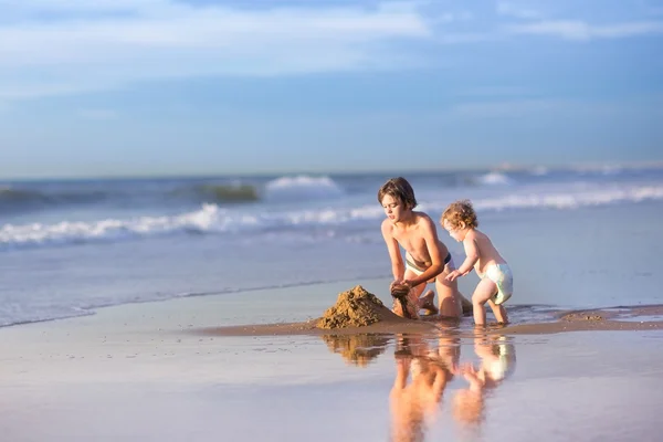 Brother and baby sister building a sand castle — Stock Photo, Image