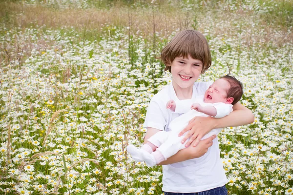 Boy holding his baby sister in a daisy field — Stock Photo, Image