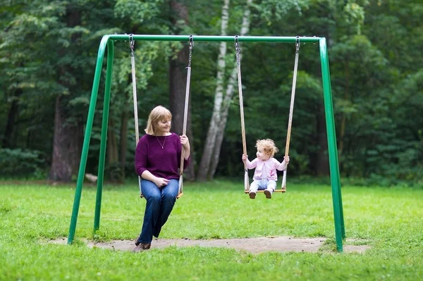 Kvinna och en liten baby flicka gungar på en playgroun — Stockfoto