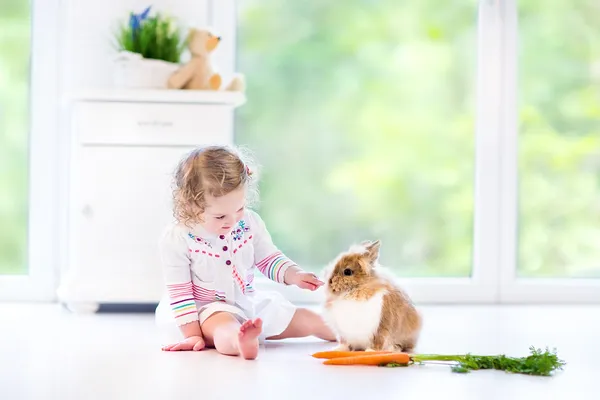 Mädchen spielt mit einem Hasen neben Blumen — Stockfoto