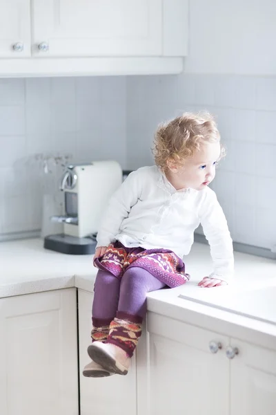 Barn flicka sitter i ett vitt kök — Stockfoto