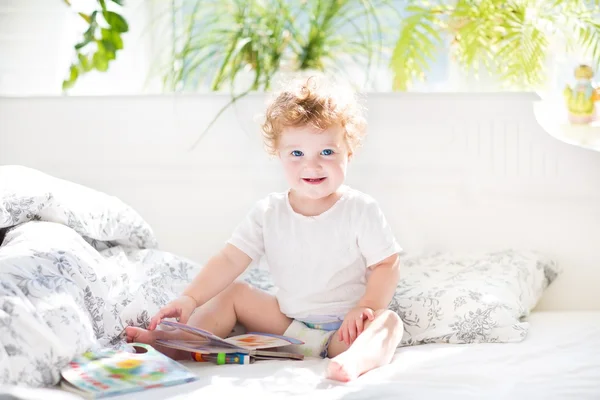 Baby lezen van een boek in haar bed van de ouders — Stockfoto