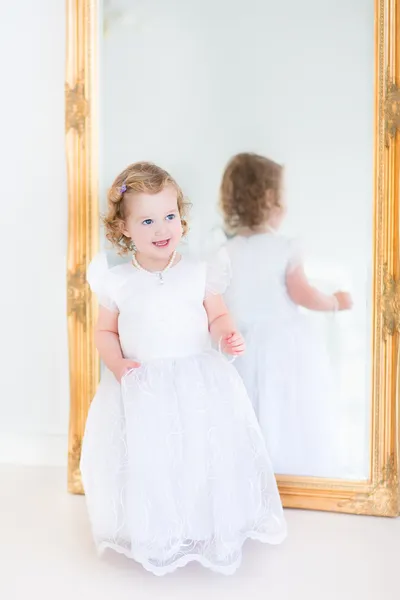 Toddler girl trying on a beautiful white dress next to a big mirror — Stock Photo, Image