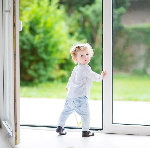 Baby flicka står vid en stor glasdörr — Stockfoto