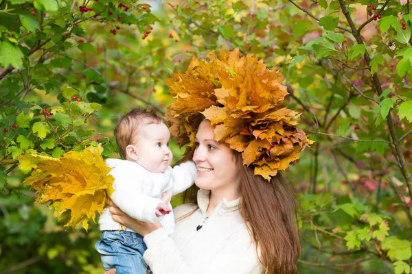 Moeder bedrijf een babymeisje met een krans van maple leaf — Stockfoto