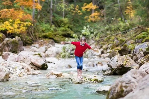 Boy trying to cross a wild mountain river jumping — Stock Photo, Image