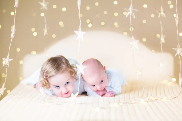 Newborn baby and toddler sister playing on a white bed — Stock Photo, Image