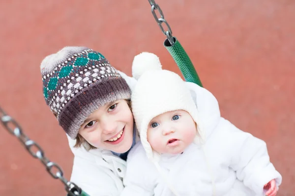 Brother and baby sister swinging in a park — Stock Photo, Image