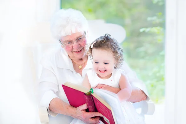 Seniorin liest ihrer kleinen Enkelin ein Buch vor — Stockfoto