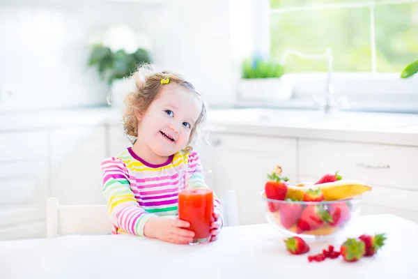 蹒跚学步的女孩吃早饭喝果汁，吃玉米片草莓 — 图库照片