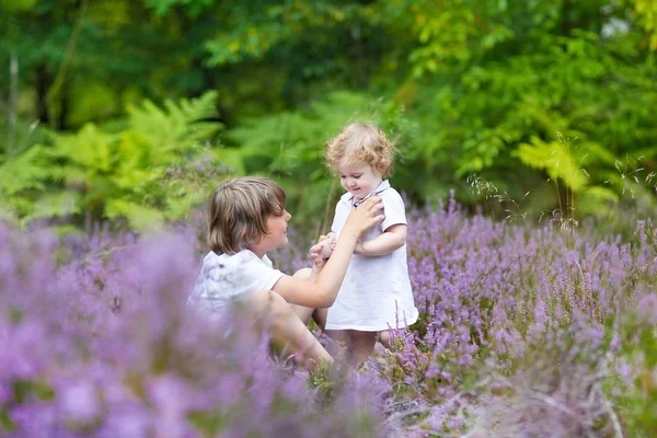 Hermano y su hermanita en hermosas flores moradas — Foto de Stock