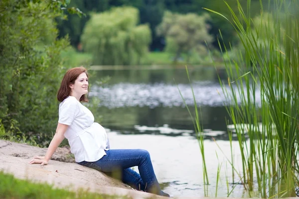 Pregnant woman relaxing at a lake shore shore — Stock Photo, Image