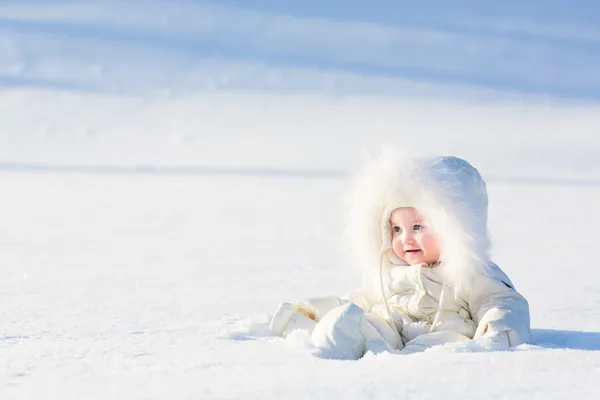 Baby in a white suit sitting in a snow field — Stock Photo, Image