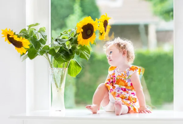 Niña sentada en una ventana junto a hermosos girasoles — Foto de Stock