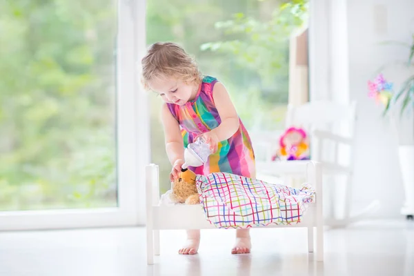 Toddler girl feeding her toy bear in a white crib — Stock Photo, Image