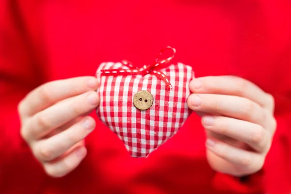Handen van een kind houden een geruite rood-witte textiel hart — Stockfoto