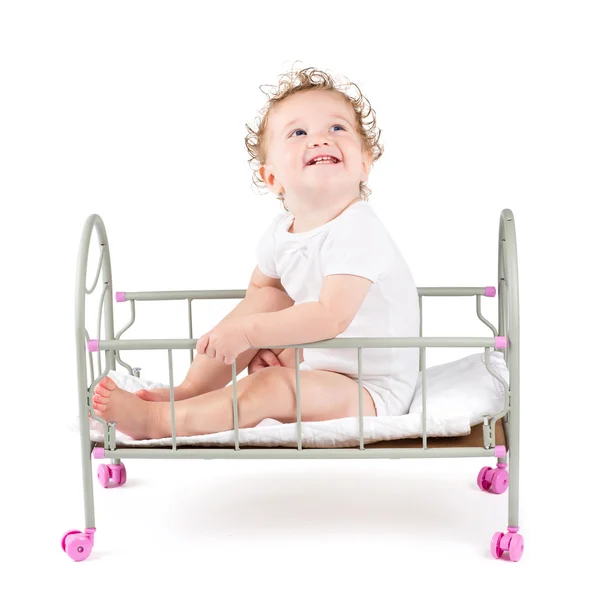 Engraçado bebê encaracolado pagando em uma cama de boneca — Fotografia de Stock