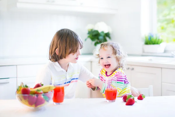 Gelukkig tiener jongen en zijn schattig peuter zus met fruit voor het ontbijt — Stockfoto